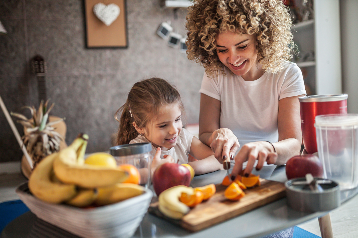 Young woman and daughter cutting up fruit on cutting board