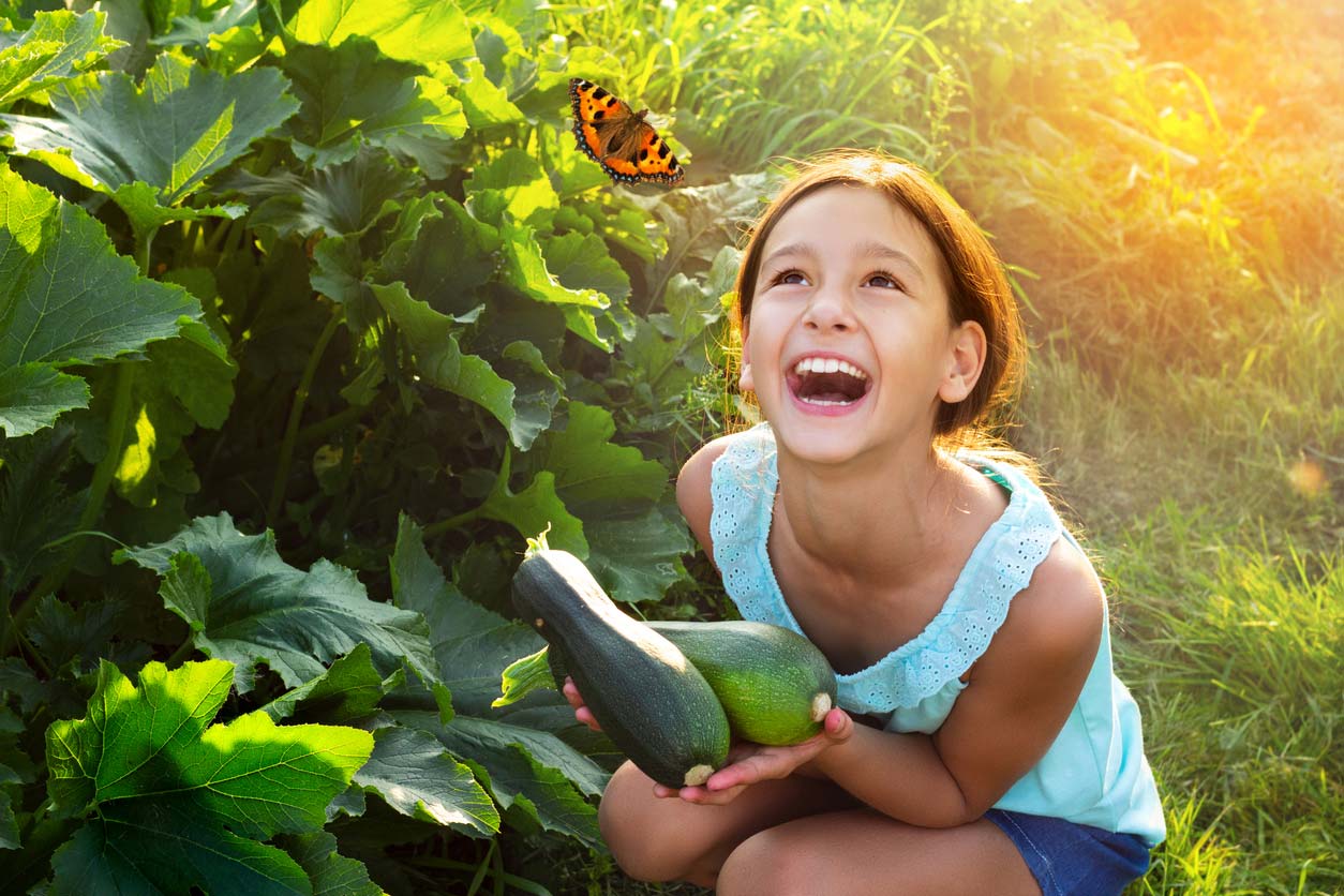 Young girl holding zucchini and looking at butterfly