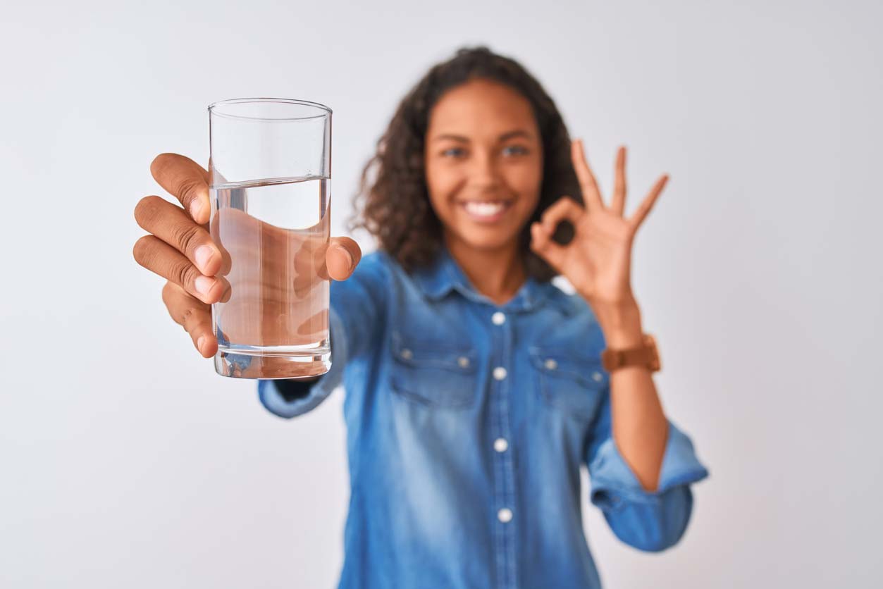 woman holding glass of water and giving okay hand gesture