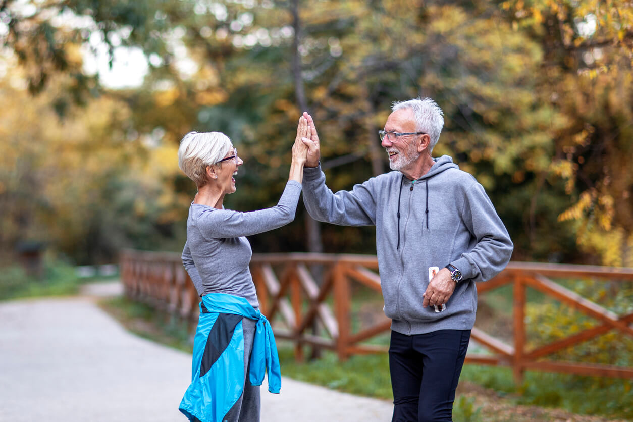 mature couple taking high five with hands after jogging in public park