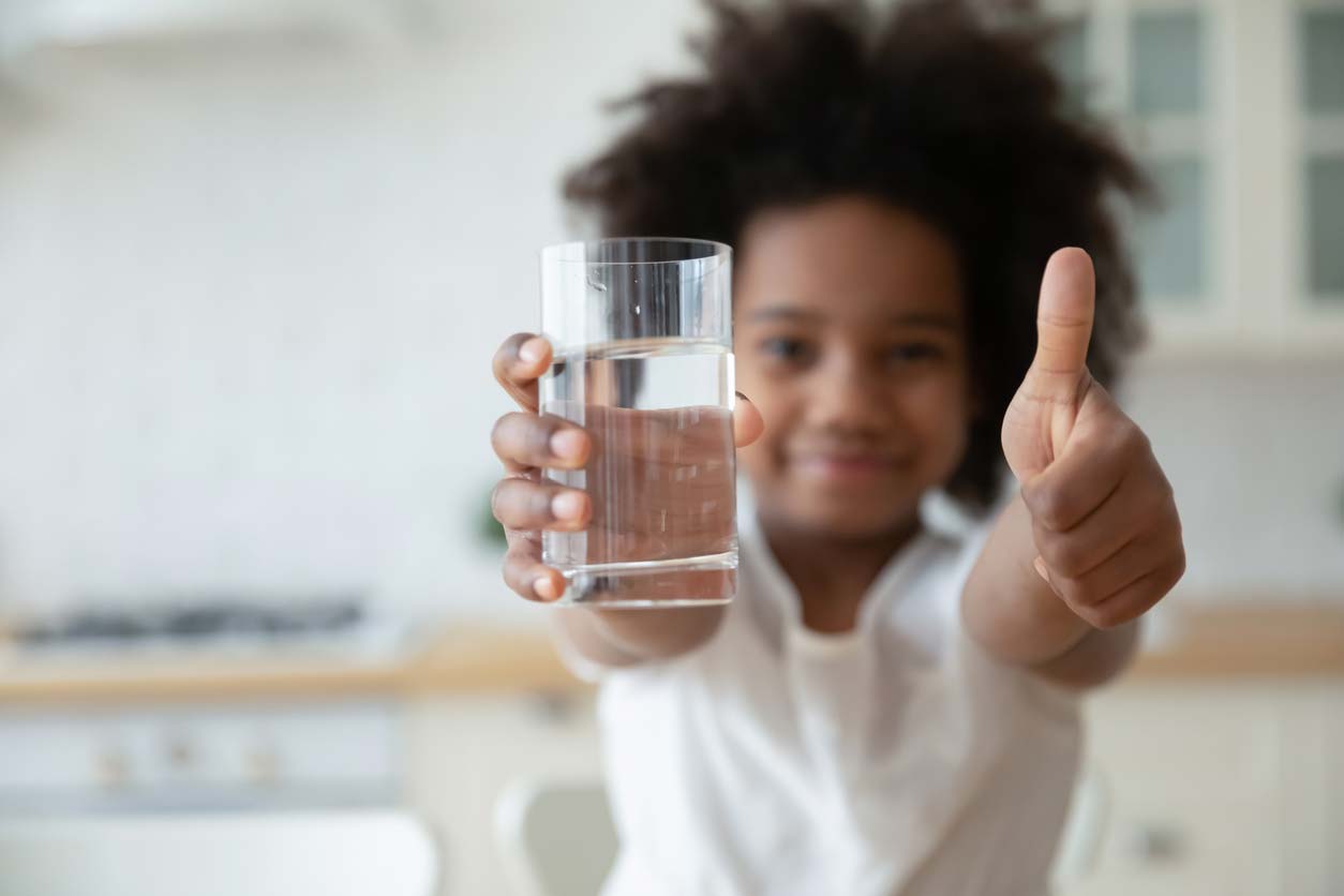 young girl holding glass of water showing thumbs up gesture