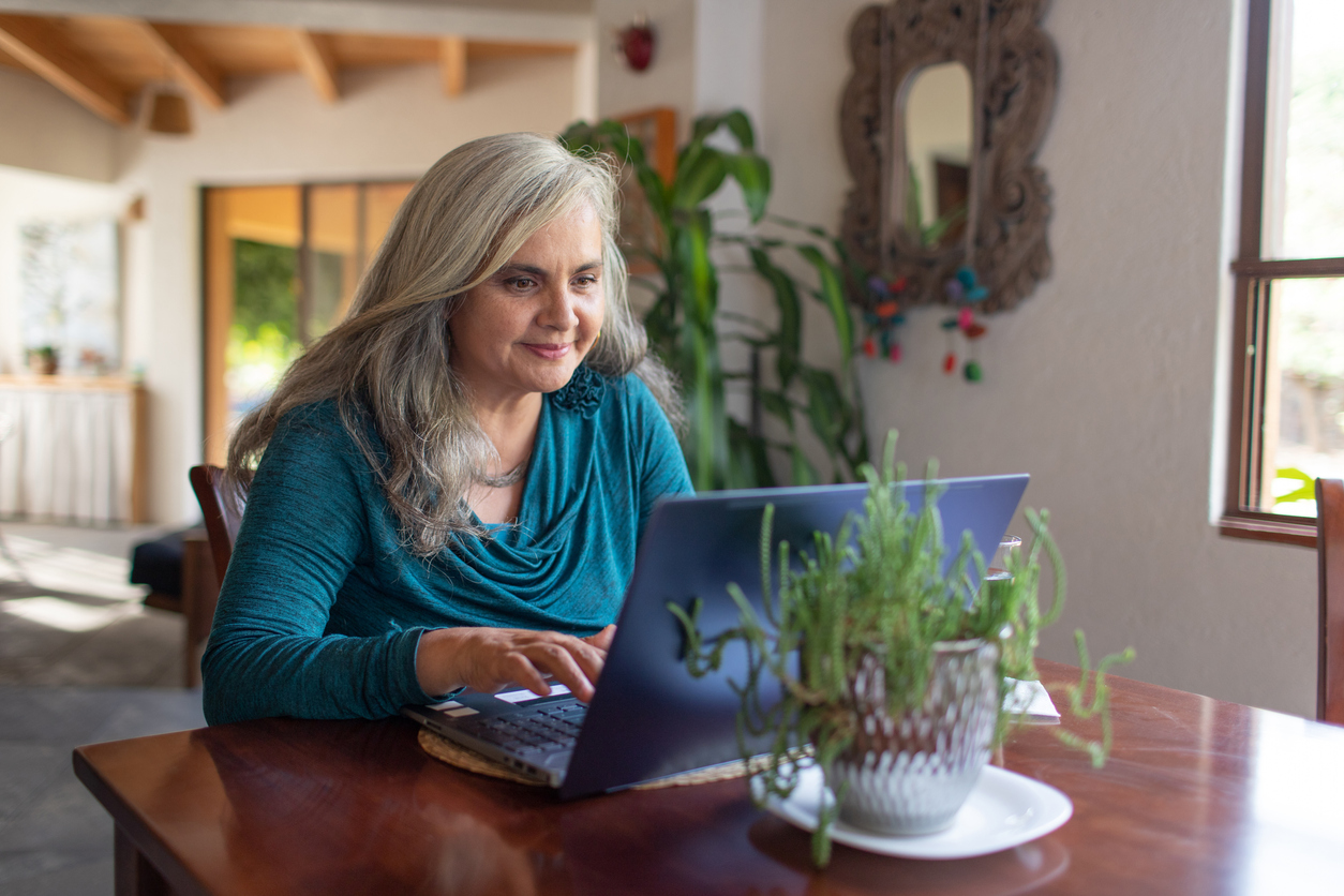 Mature woman with long gray hair  working on laptop from home, smiling
