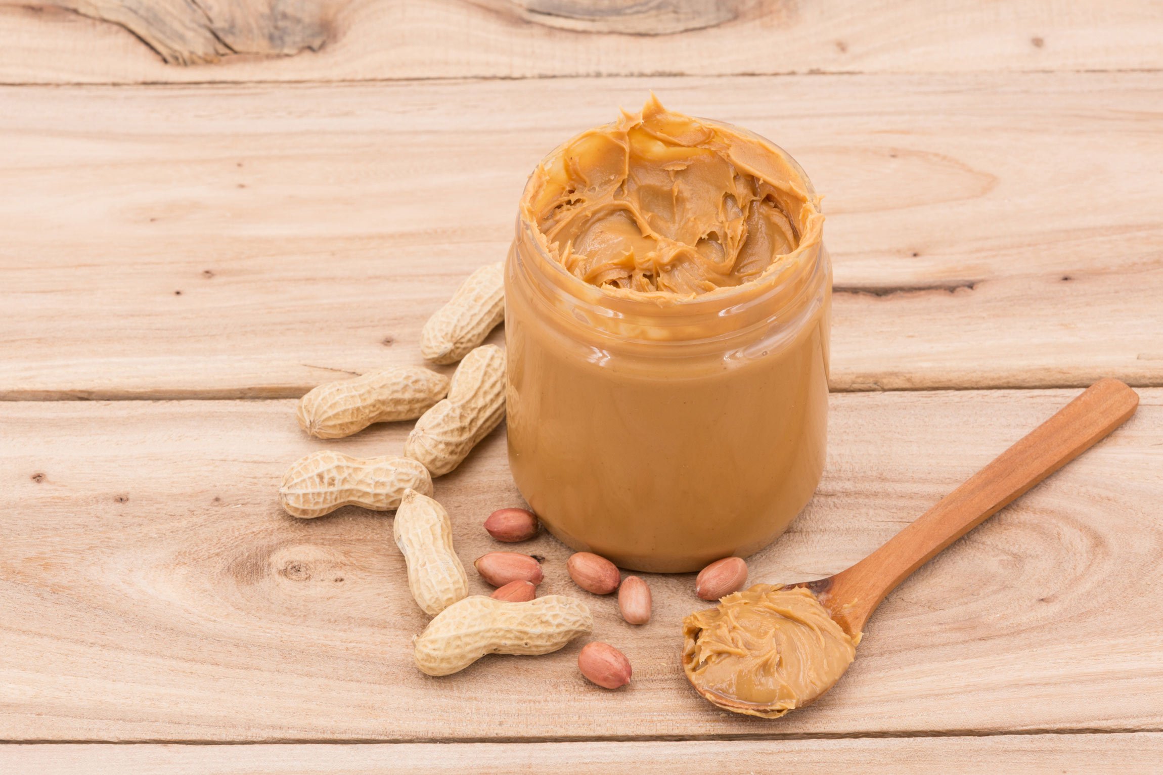 A jar of peanut butter with peanuts on a wooden table